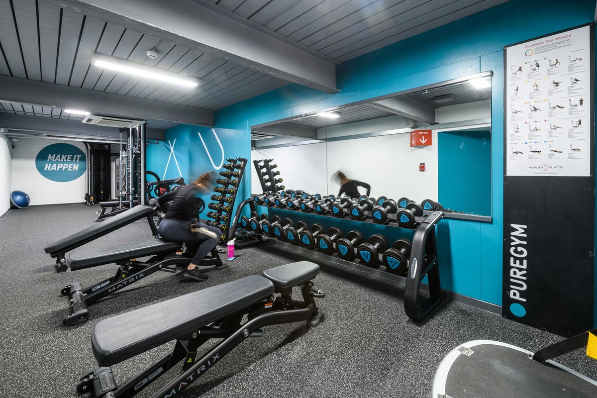 PureGym Northampton Central: Benches, dumbbell racks, rubberized flooring, and teal-coloured accent walls in a gym studio.