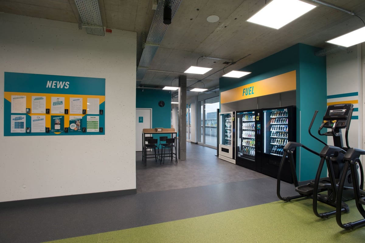 PureGym Adliswil: Salles de sport avec tableau d'actualités, chaises et tables et distributeurs automatiques.