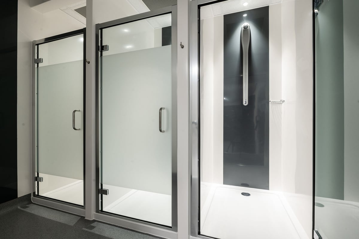 PureGym Cirencester: Shower stalls with frosted glass doors and tiled flooring.