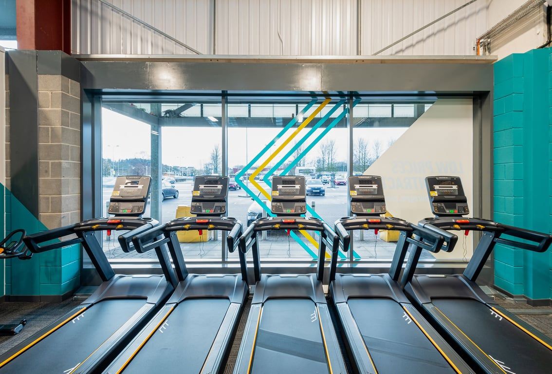 PureGym Elgin: Rows of treadmills facing large windows overlooking cityscape.
