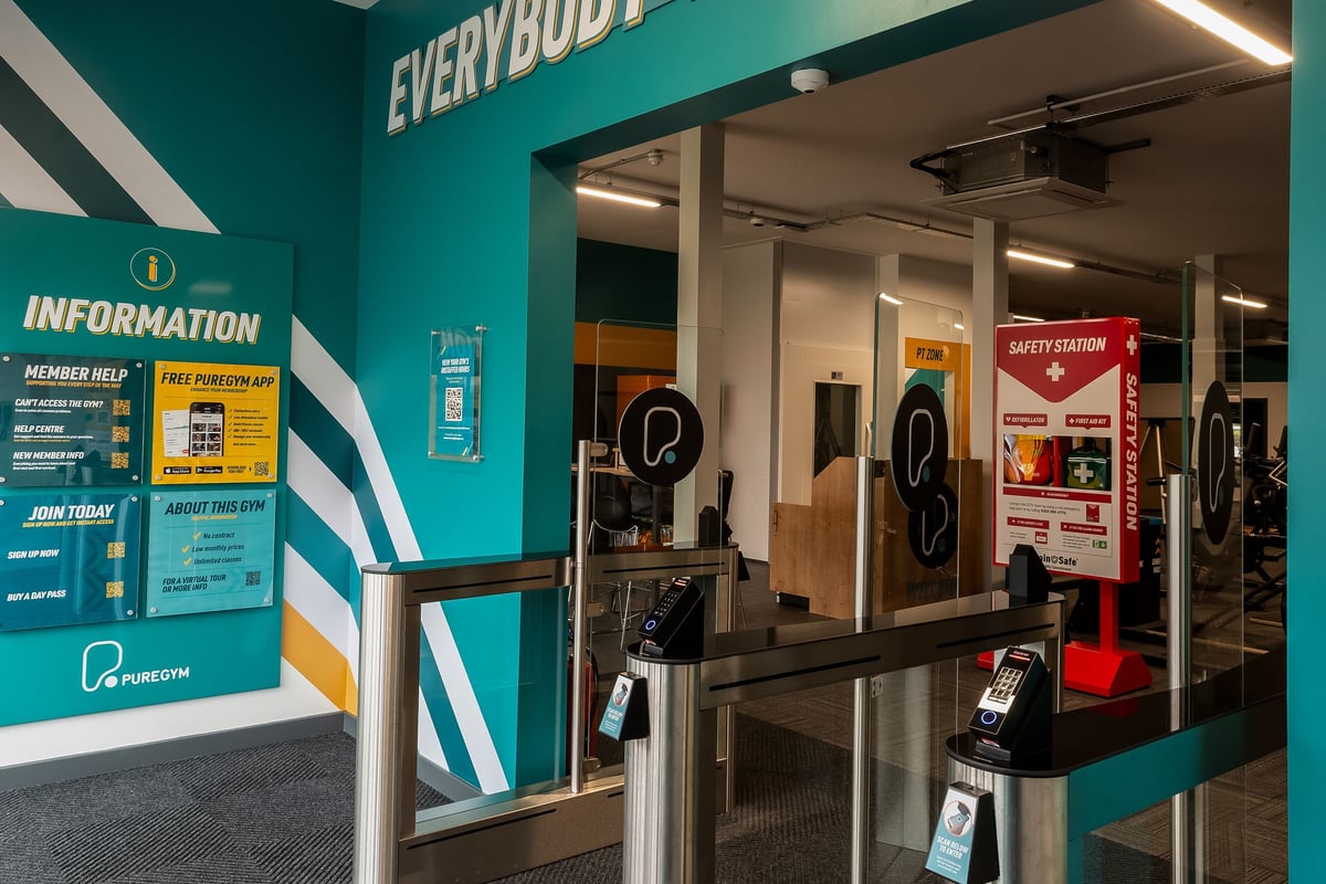 PureGym Llantrisant: Entrance area with information desk, turnstiles, safety signage.