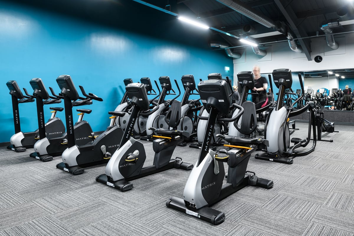 PureGym Southend Fossetts Park: Rows of stationary bikes in a dimly lit gym space with blue-tinted lighting.