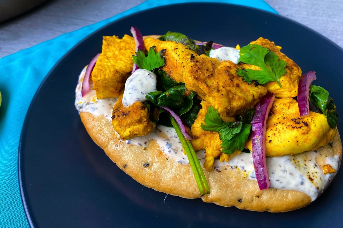 Flatbread topped with spiced chicken, vegetables and herbs on a dark plate