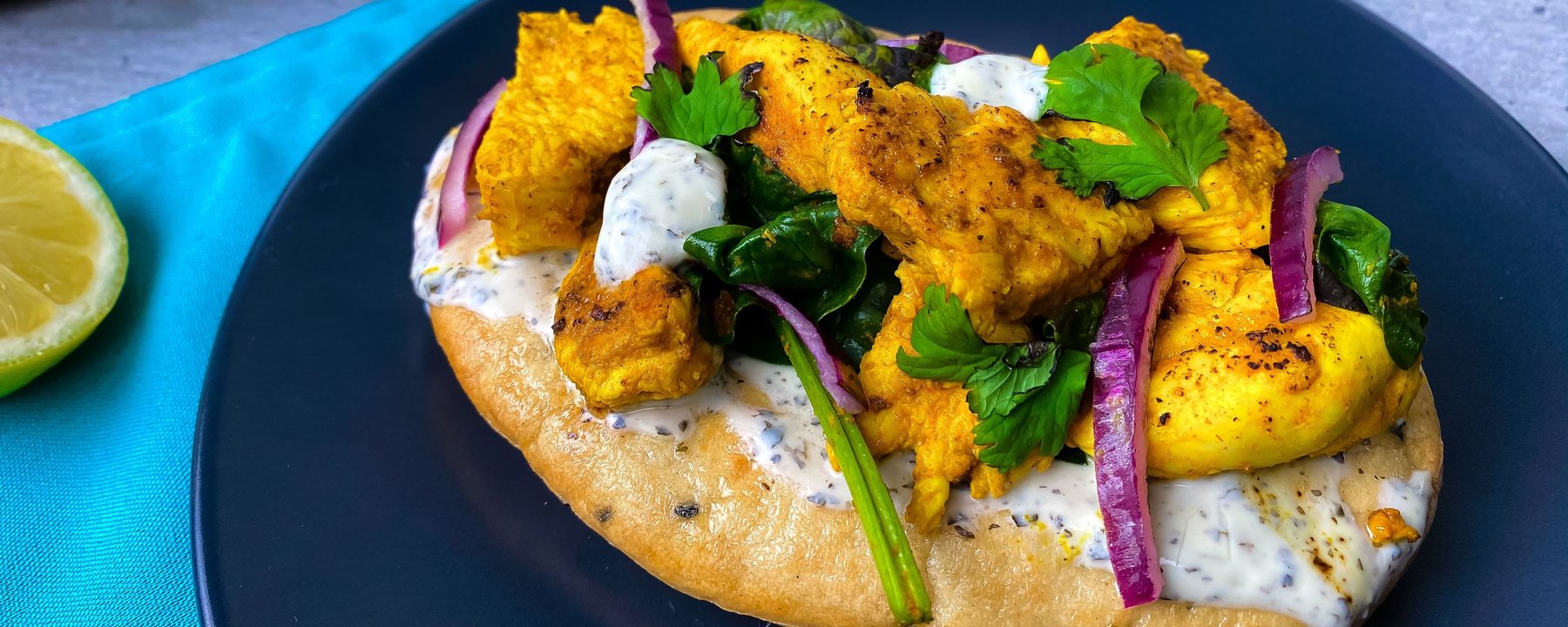 Flatbread topped with spiced chicken, vegetables and herbs on a dark plate