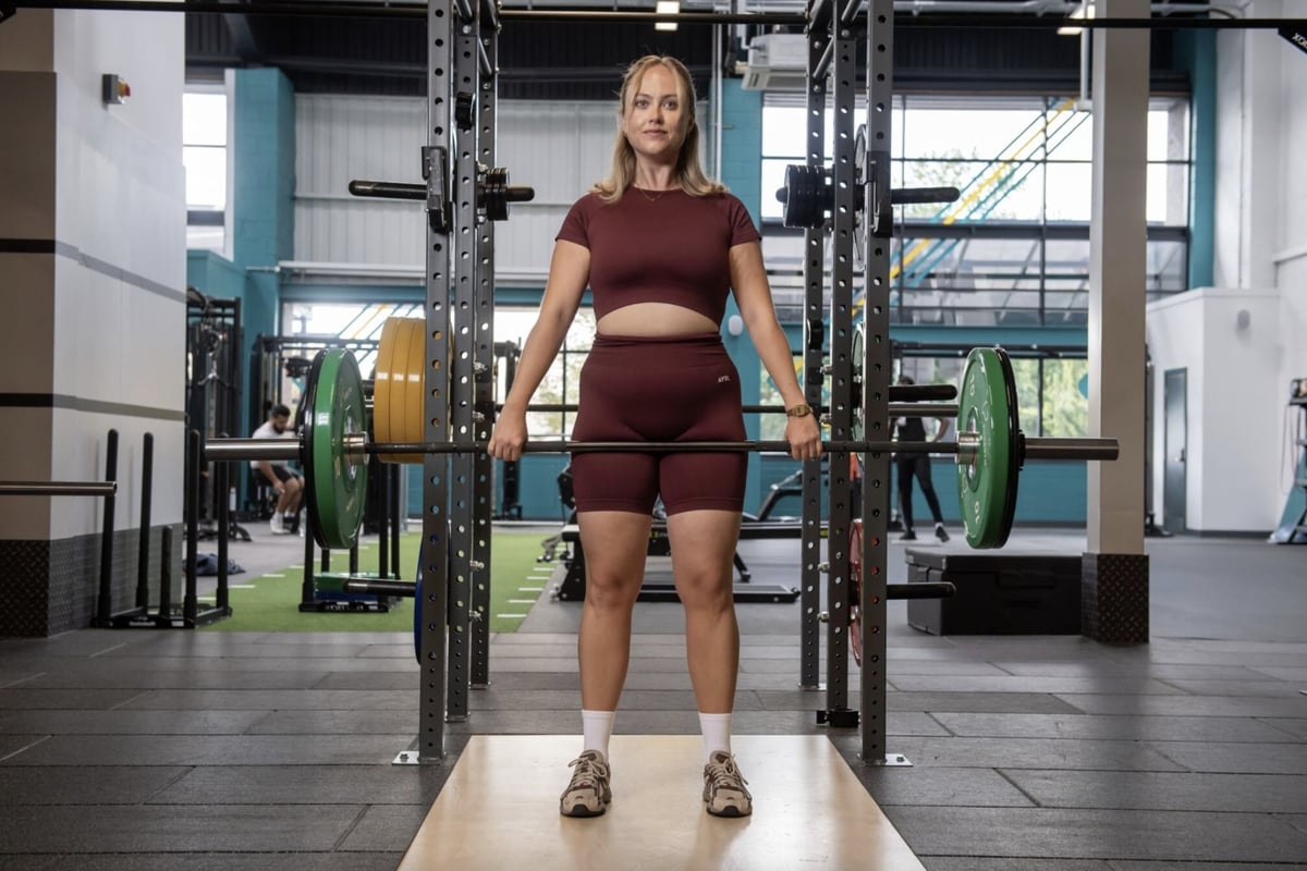 Woman in burgundy sportswear lifting a barbell with green weights in a gym