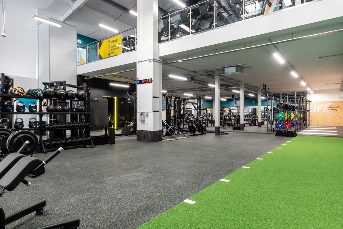 PureGym Kettering: Gym interior with weight racks, resistance machines, rubberized flooring, and colourful graffiti mural.