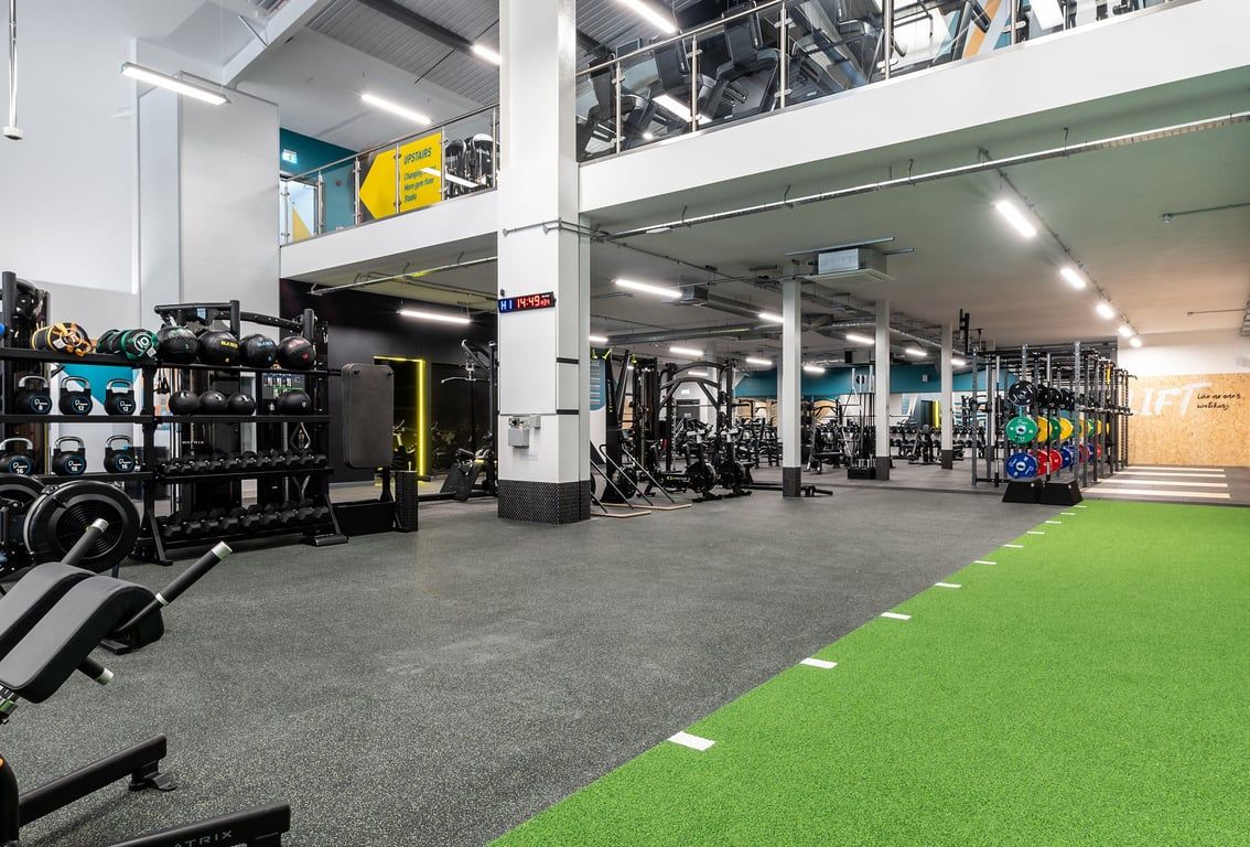 PureGym Kettering: Gym interior with weight racks, resistance machines, rubberized flooring, and colourful graffiti mural.