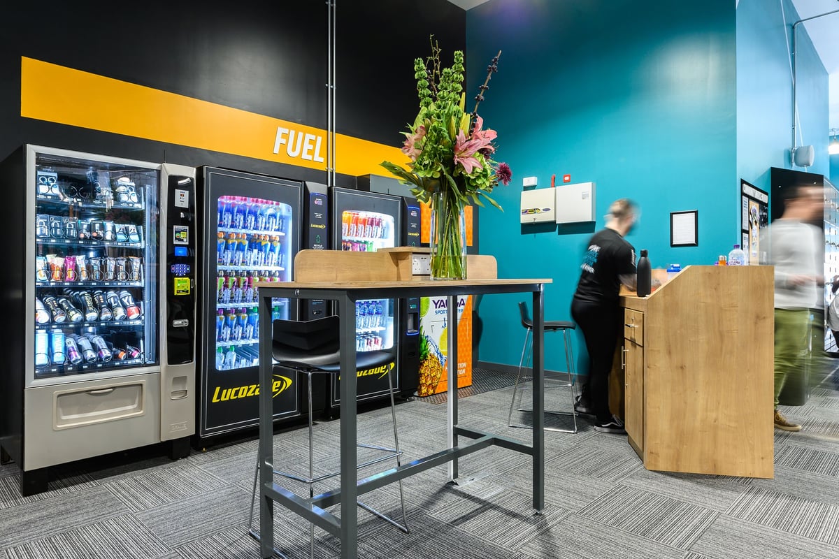 PureGym Bath Spring Wharf: Vending machines, high stools, and a table in a teal room.
