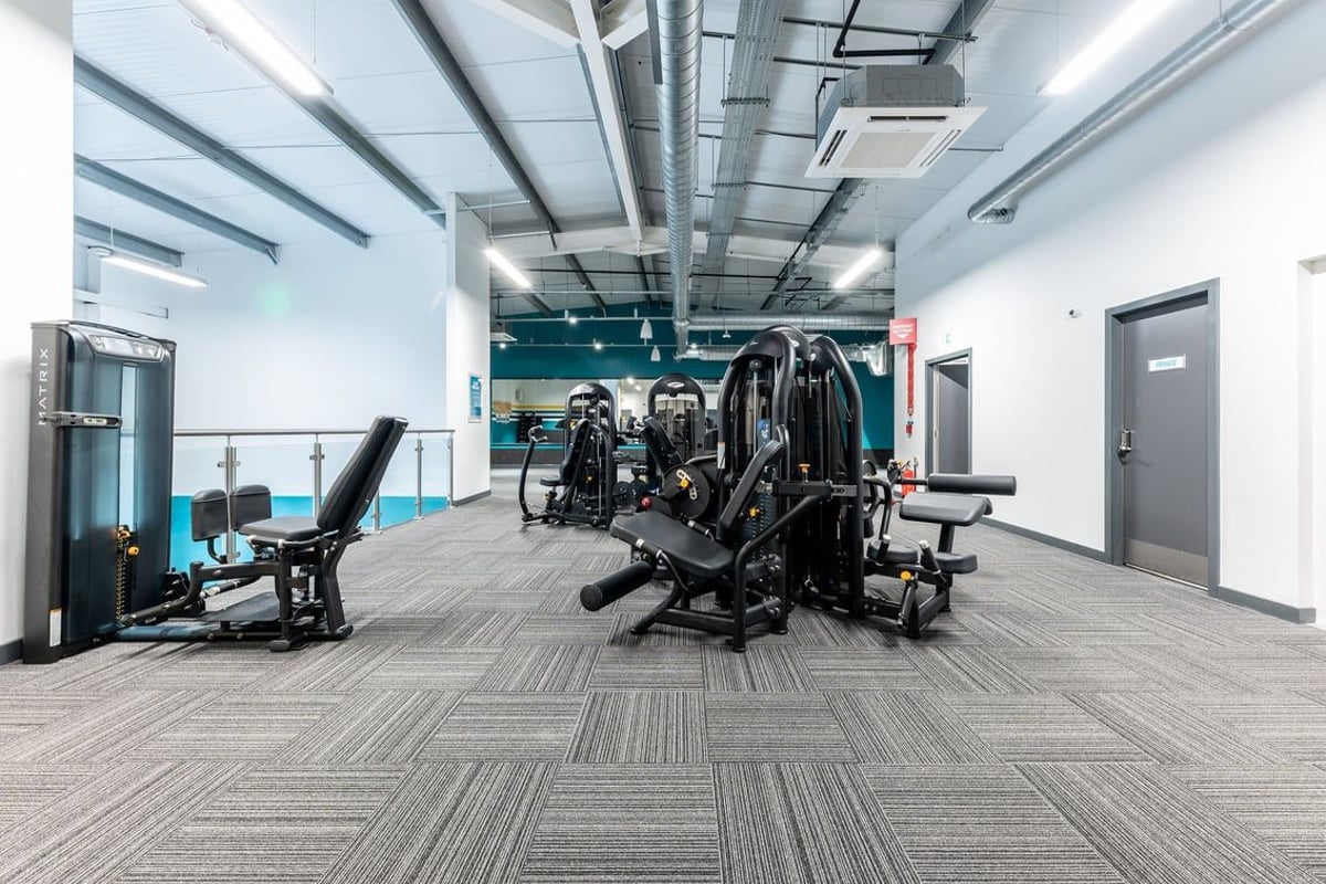 PureGym Galashiels: Strength training area with weight machines, benches, and rubberized flooring.