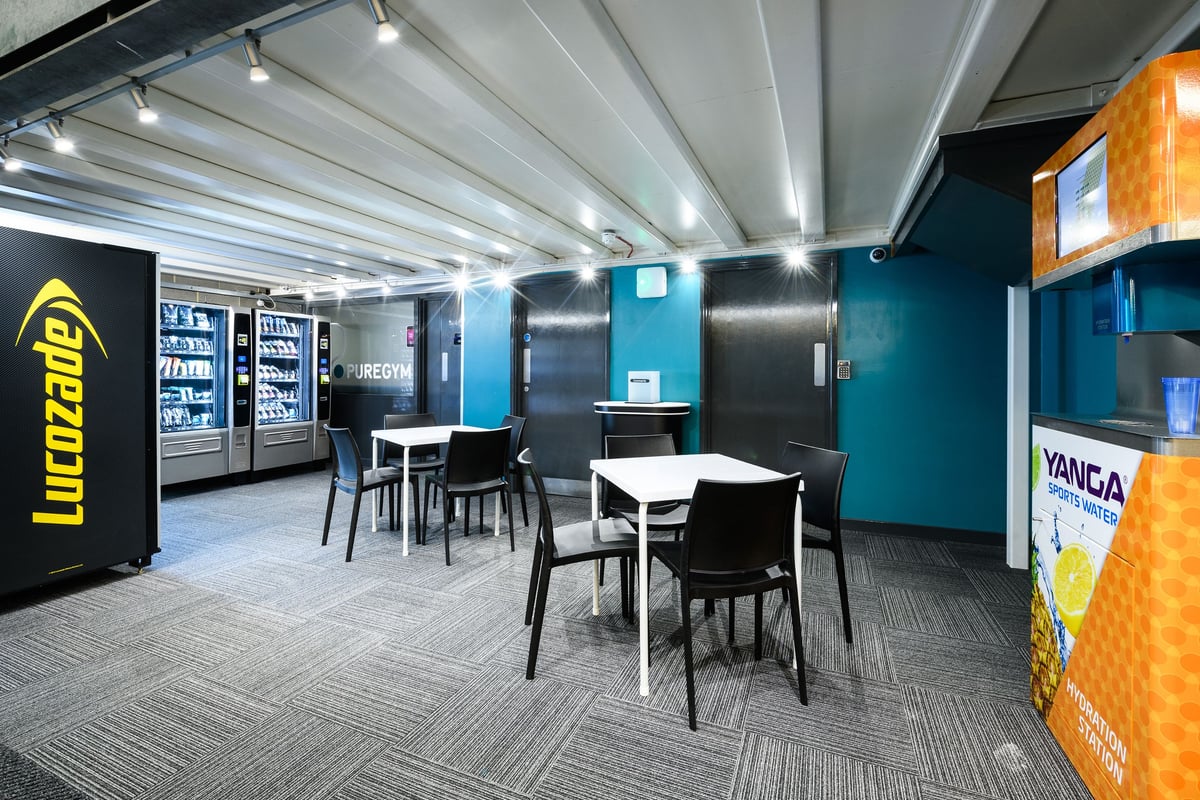 PureGym London Borough: Vending machines, furniture, and teal walls in what seems to be a break room or lounge area.