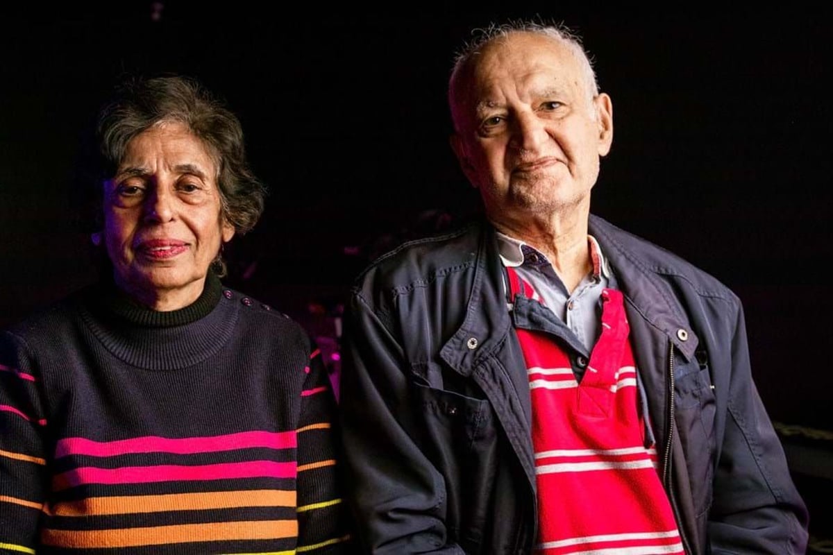 Elderly man and woman sitting side by side against a dark background