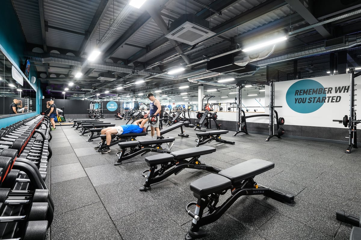 PureGym Leeds Thorpe Park: Rows of weight benches, squat racks, free weights, rubberized flooring, and motivational signage.