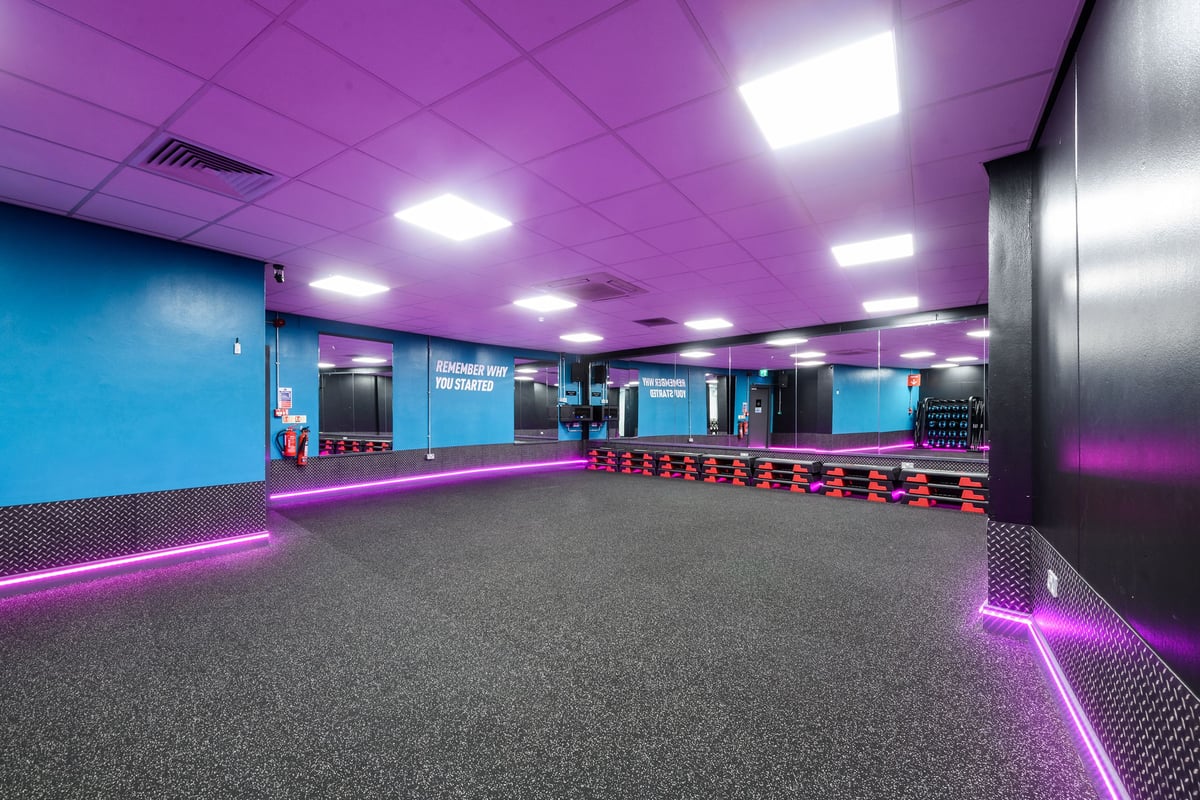 PureGym London Wandsworth: Mirrored walls, rubberized flooring, vivid purple and blue lighting, exercise studio aesthetic.