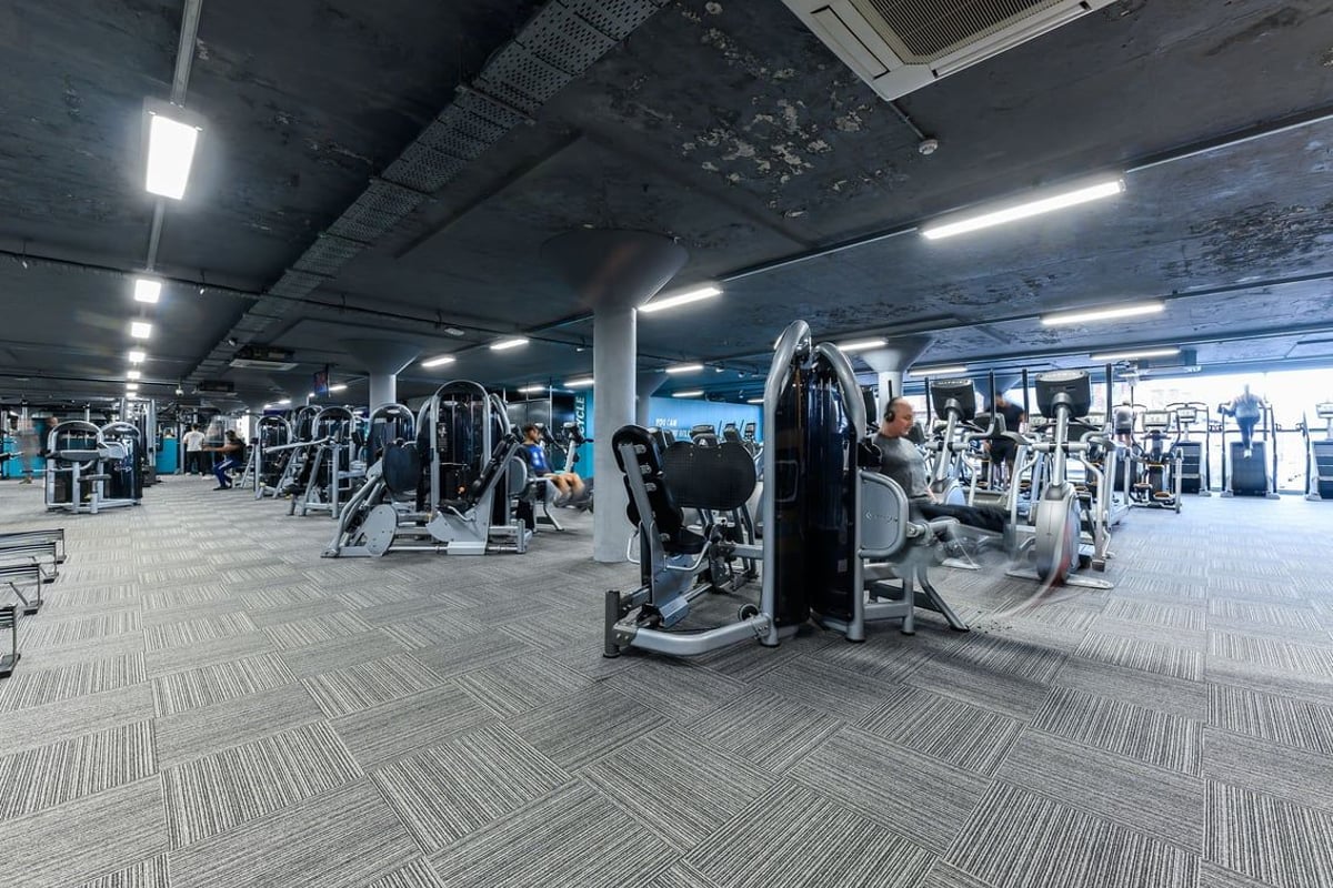 PureGym Nottingham Basford: Rows of weight machines, benches, and rubberized flooring in a dimly lit gym interior.