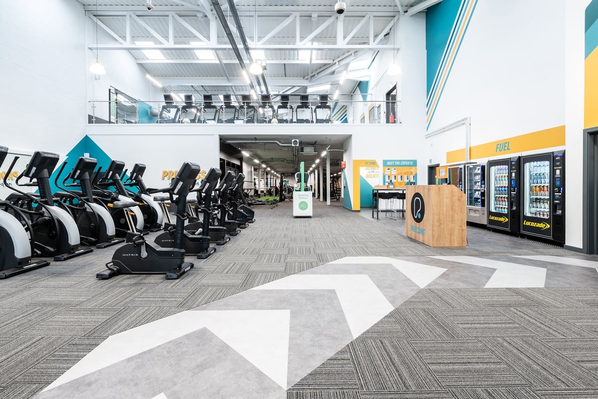 PureGym Yeovil Houndstone Retail Park: Rows of stationary bikes and treadmills in a bright gym with vending machines nearby.