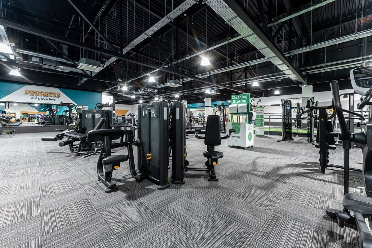 PureGym Bracknell: Weight machines, cable crossover stations, free weights, and rubberized flooring in a dimly lit gym.