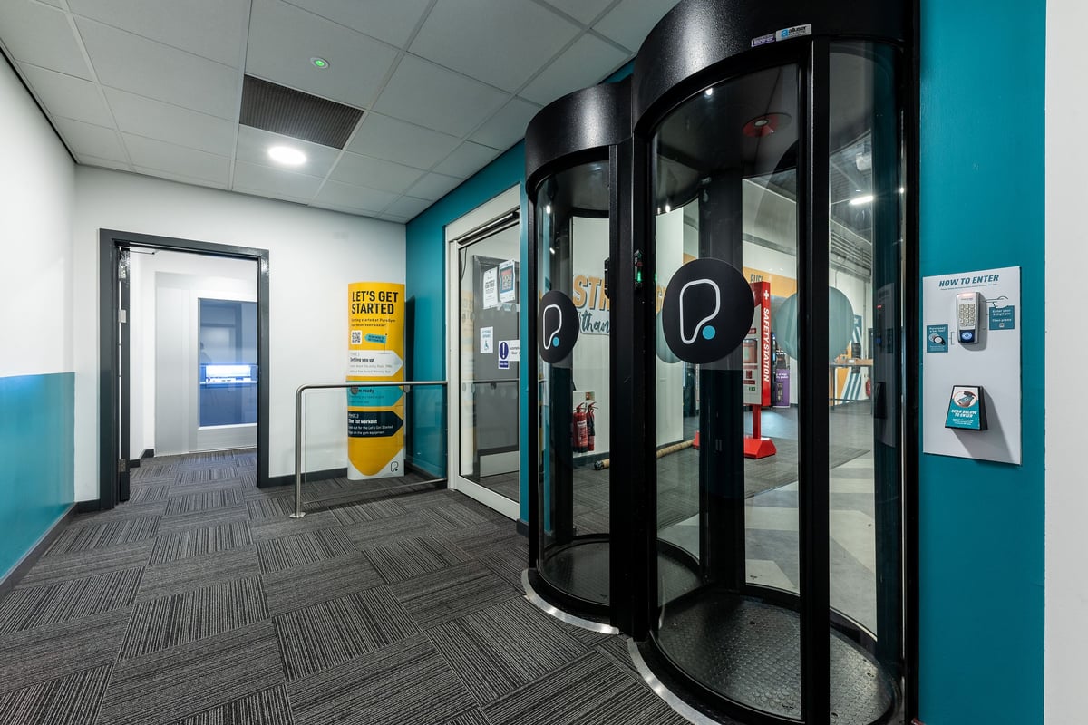 PureGym Chatham: Revolving doors, vending machines, wall adverts in a gym entry or lobby area.