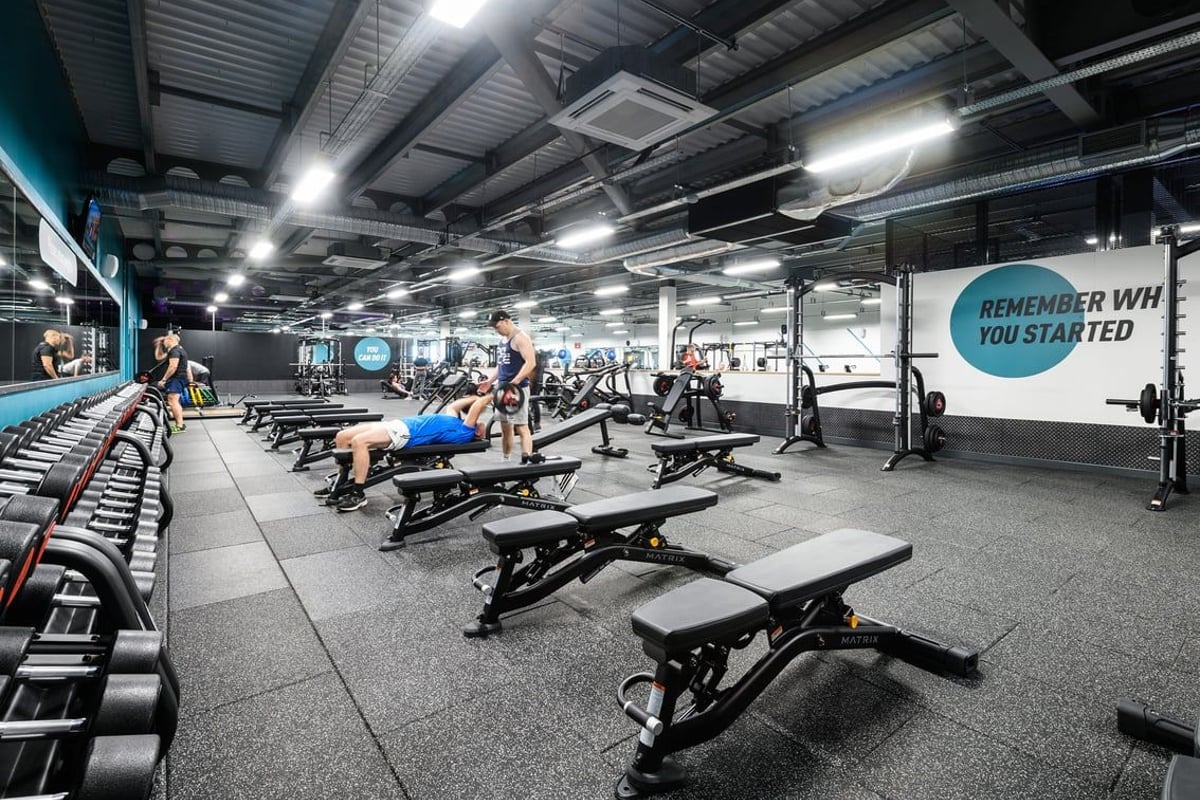 PureGym Leeds Thorpe Park: Rows of weight benches, squat racks, free weights, rubberized flooring, and motivational signage.
