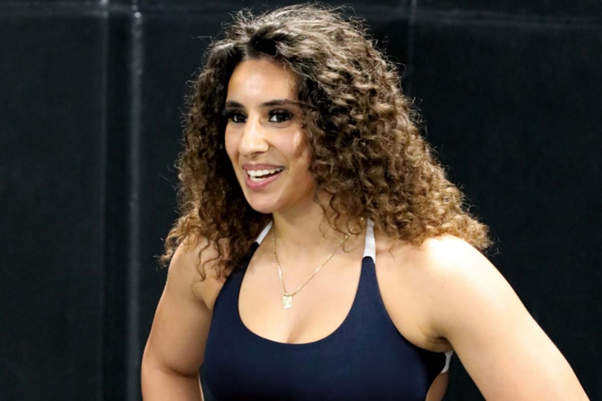 Smiling woman with curly hair wearing a navy blue sports top against a dark background