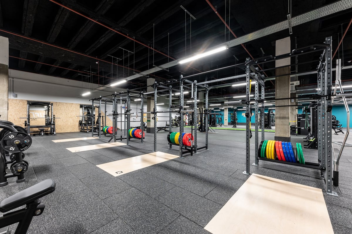 PureGym London Stratford: Gym interior with weight racks, barbells, bumper plates, squat racks, and rubberized flooring.