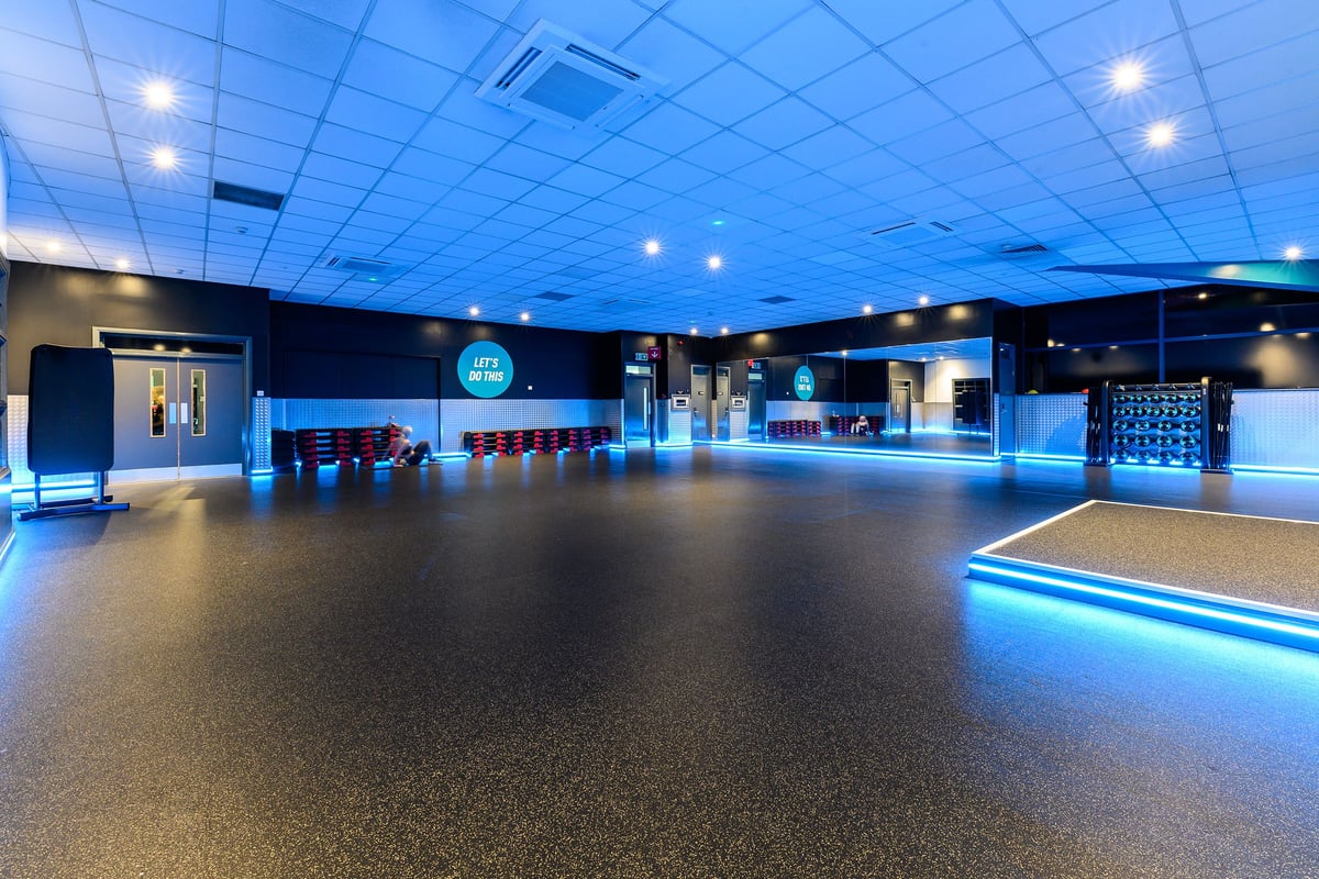 PureGym Mansfield: Large empty gym studio with blue lighting, rows of benches, and rubberized flooring.