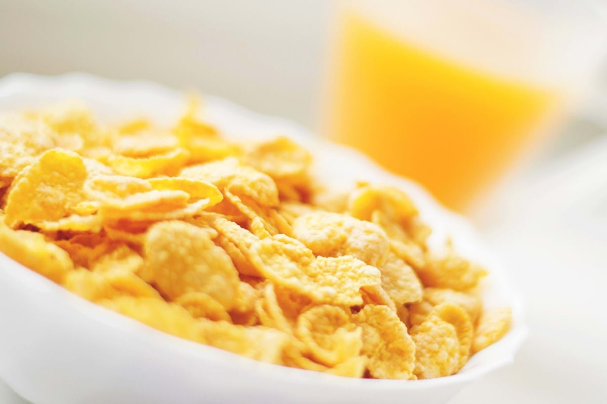 Cornflakes in a white bowl with a glass of orange juice in the background