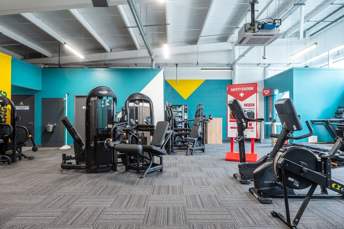 PureGym Bideford: Strength machines, cardio equipment, weight racks, and teal-yellow walls with motivational signage.