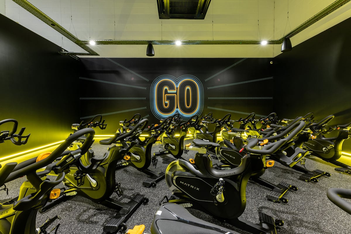 PureGym Watford Waterfields Retail Park: Rows of stationary exercise bikes in yellow and black, "GO" signage on the wall.