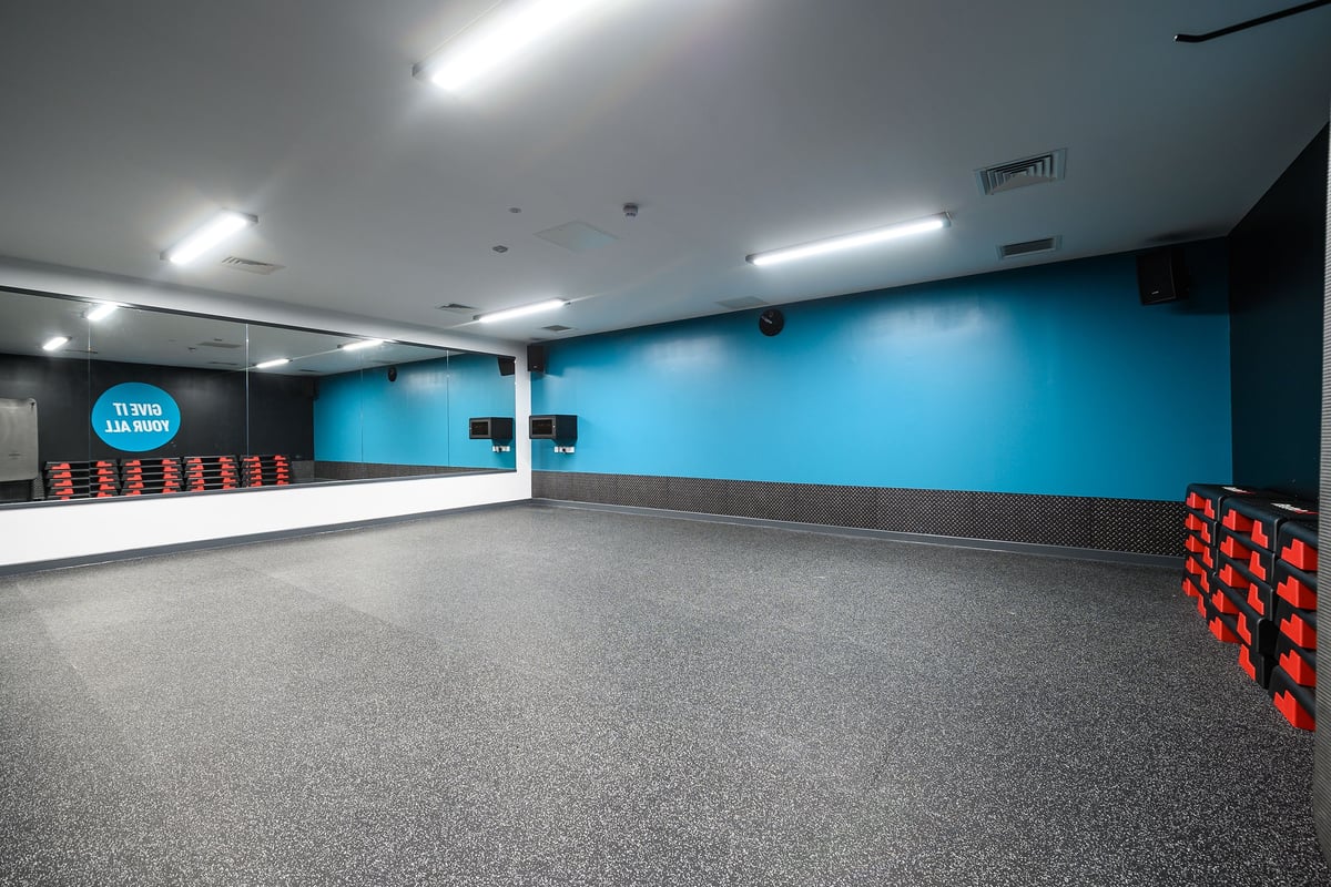 PureGym Glossop: Black padded boxes alongside a teal wall, mirrored surfaces, and rubberized flooring.