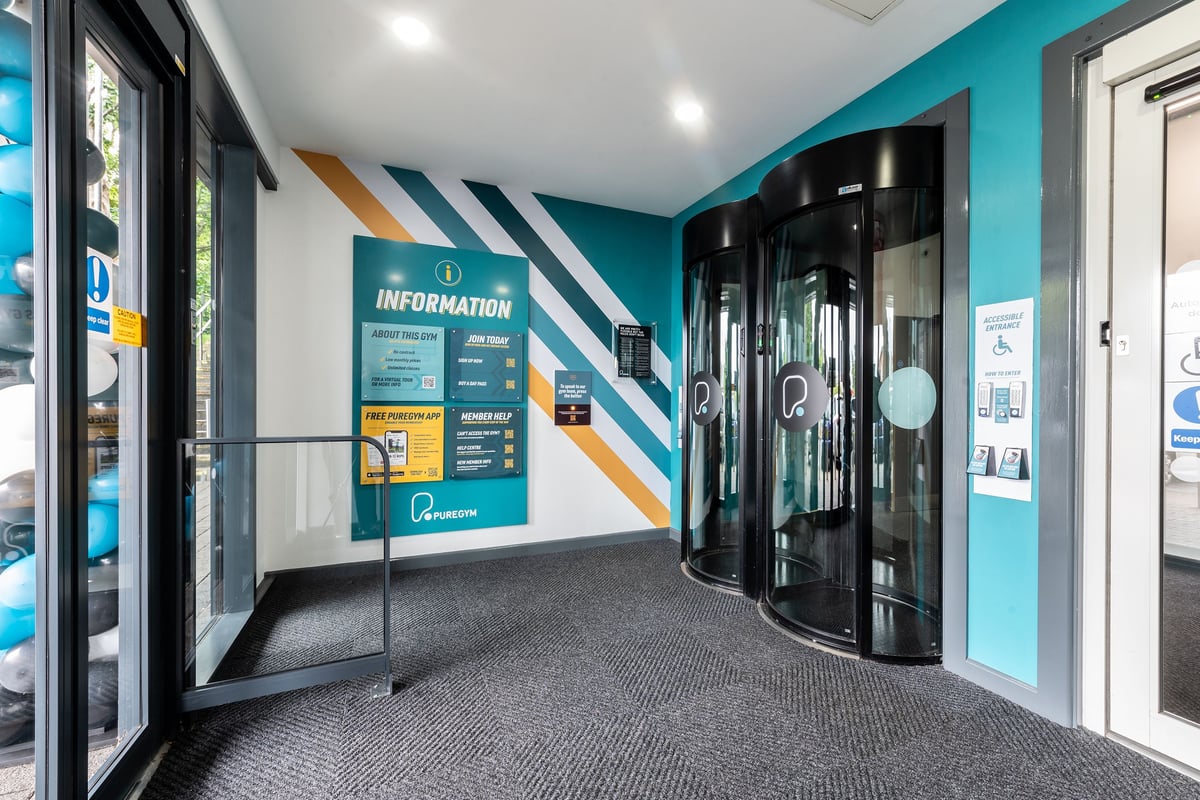 PureGym Banbury Cross Retail Park: Revolving door entrance, information signage, and teal branding accents.