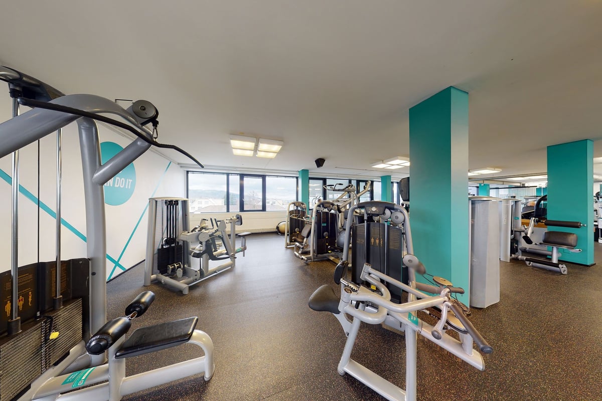 PureGym Dietikon: Exercise machines, weight racks, and teal accented mirrored walls.