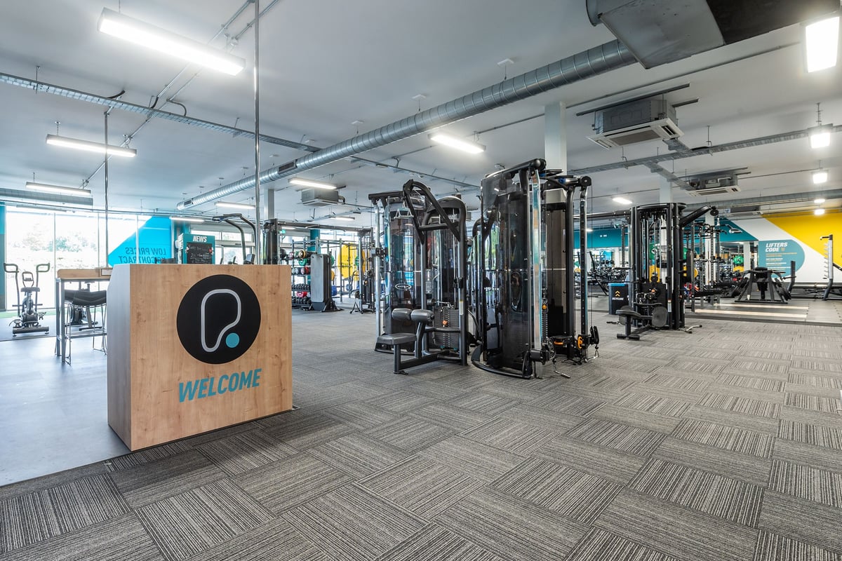 PureGym Wirral Bidston Moss: Weight machines, resistance equipment, wall-mounted televisions, and a patterned floor.