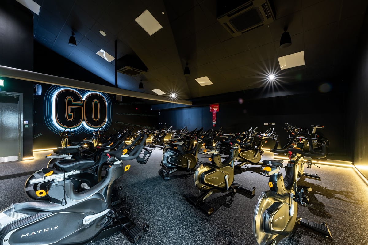 PureGym Bangor Northern Ireland: Rows of stationary exercise bikes in a dimly lit studio with neon 'GO' signage.