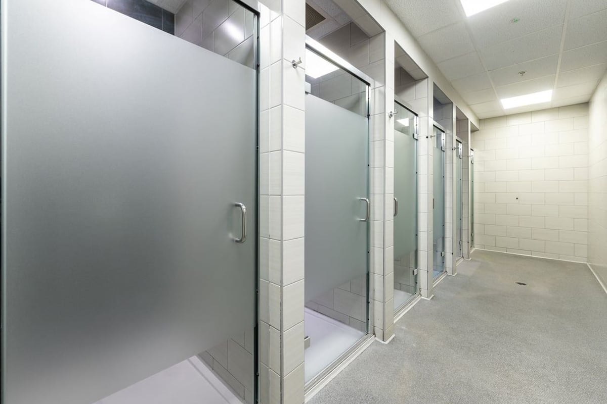 PureGym Ipswich Buttermarket: Rows of glass-enclosed shower cubicles in a tiled facility.