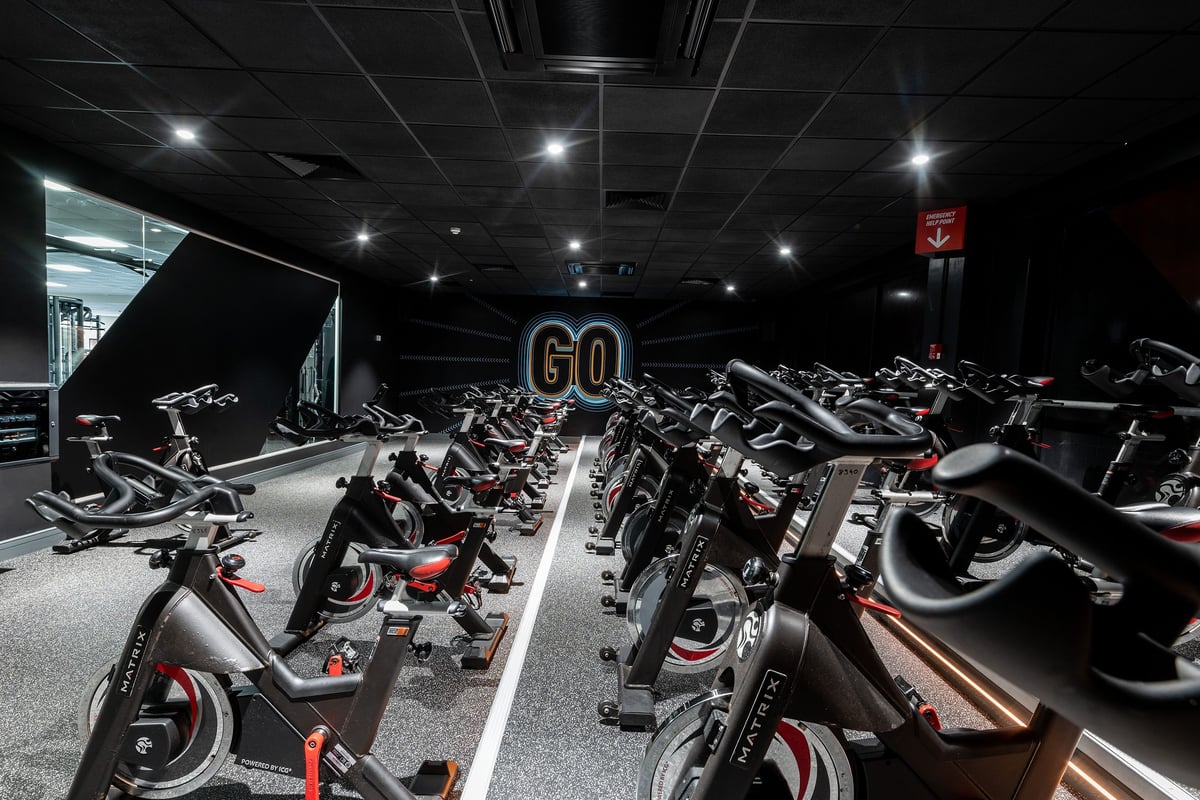 PureGym Woking: Rows of stationary bikes arranged on rubberized flooring in a dimly lit fitness studio.