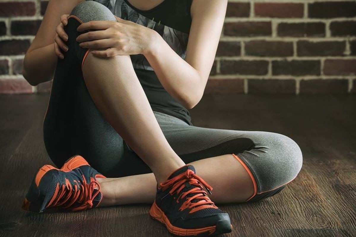 Person in sportswear sitting on wooden floor against brick wall holding knee