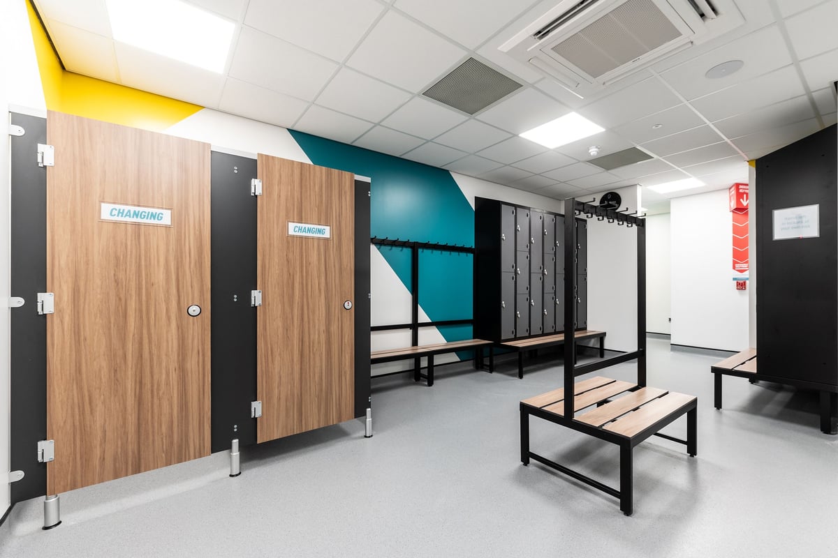 PureGym Derby Meteor Centre: Changing cubicles, benches, and lockers in a functional changing area.