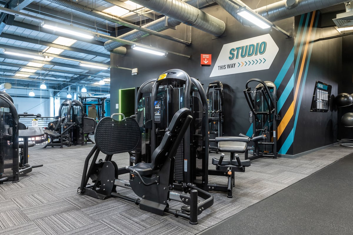 PureGym Aintree: Rows of black strength training machines, mirrors, tubing, free weights, and rubberized flooring.