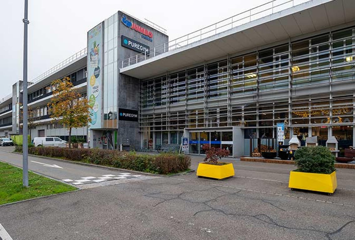 Puregym Volketswil: Grosse Ladenfront mit Parkplatz, Pflanzgefässe im Vordergrund.