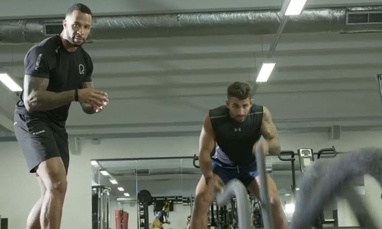 Two men exercising with battle ropes in a gym with mirrors and equipment behind them