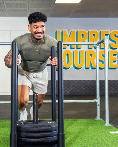 Mann schiebt einen Gewichtsschlitten mit «Impress Yourself» Text an der Gym-Wand