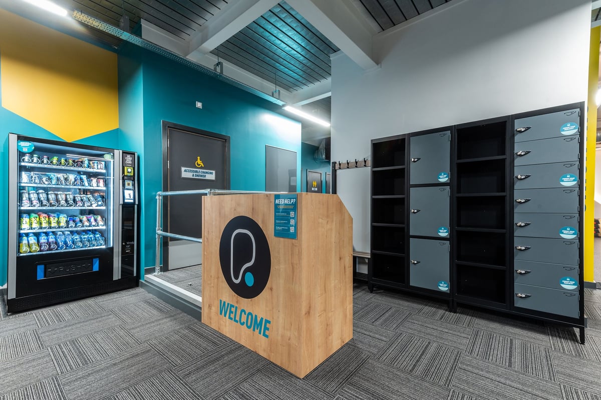PureGym Droitwich Spa: Vending machine, lockers, wooden welcome sign in a colourful interior space.