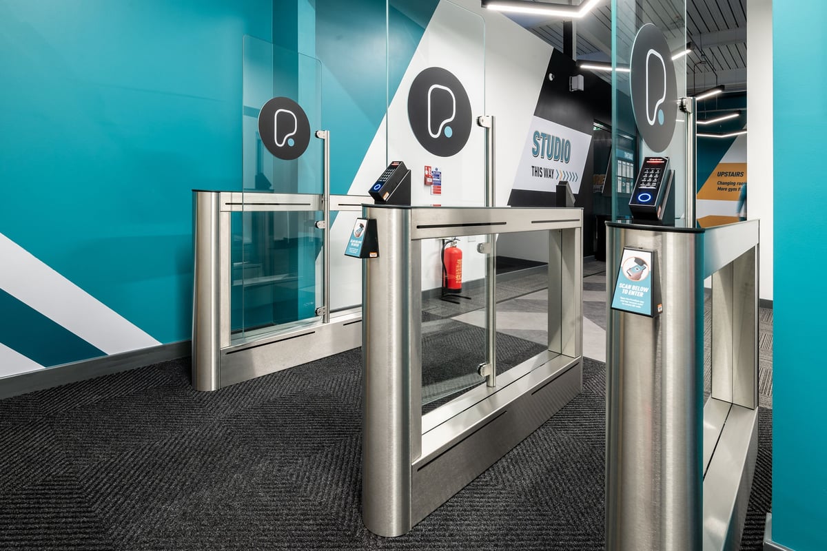 PureGym London Colney: Silver turnstiles, blue branding, and what appears to be a studio entrance area.