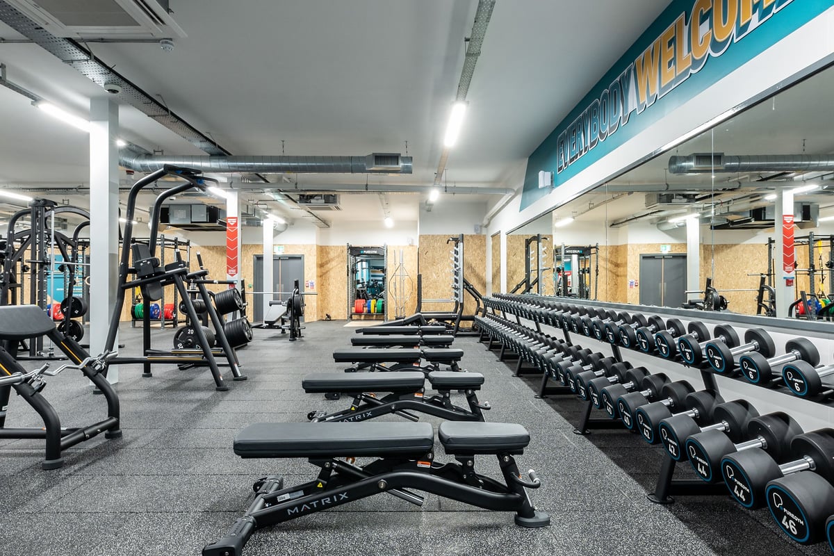 PureGym Boston: Weightlifting area with squat racks, benches, dumbbells, weight plates, and rubberized flooring.
