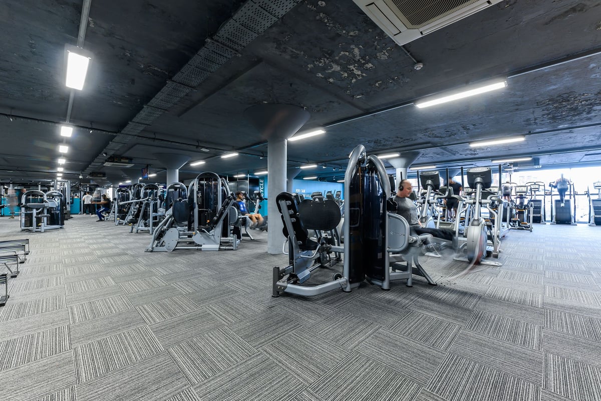 PureGym Nottingham Basford: Rows of weight machines, benches, and rubberized flooring in a dimly lit gym interior.