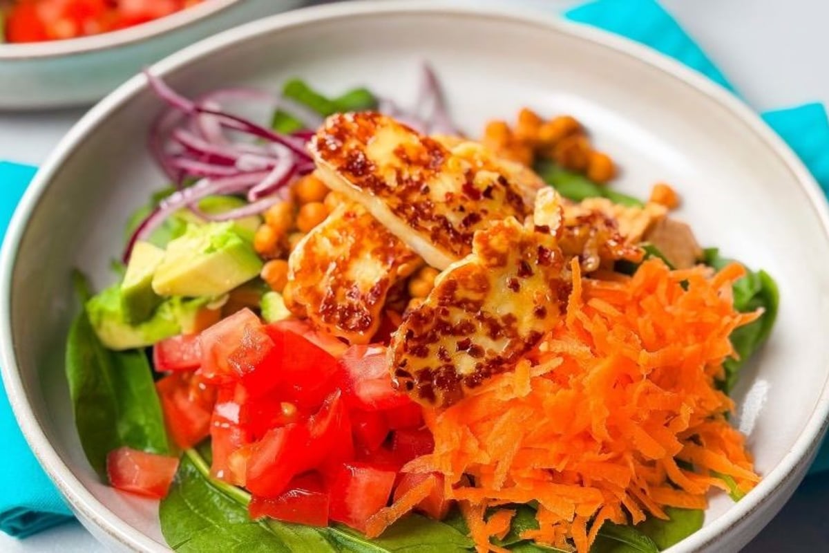 Salad with grilled halloumi, shredded carrot, diced tomato, avocado, spinach, and red onion