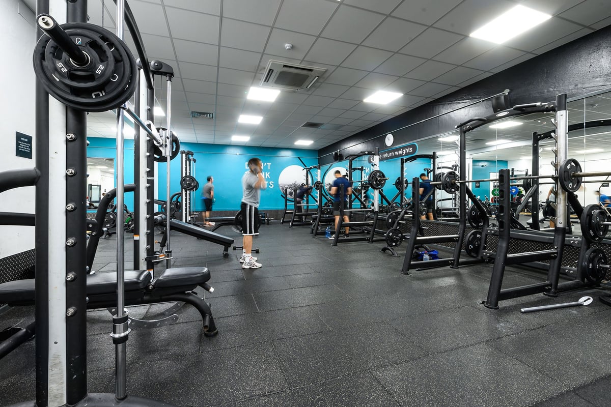 PureGym Burnham: Squat racks, weight plates, benches, rubberized flooring in a gym with teal accent walls.