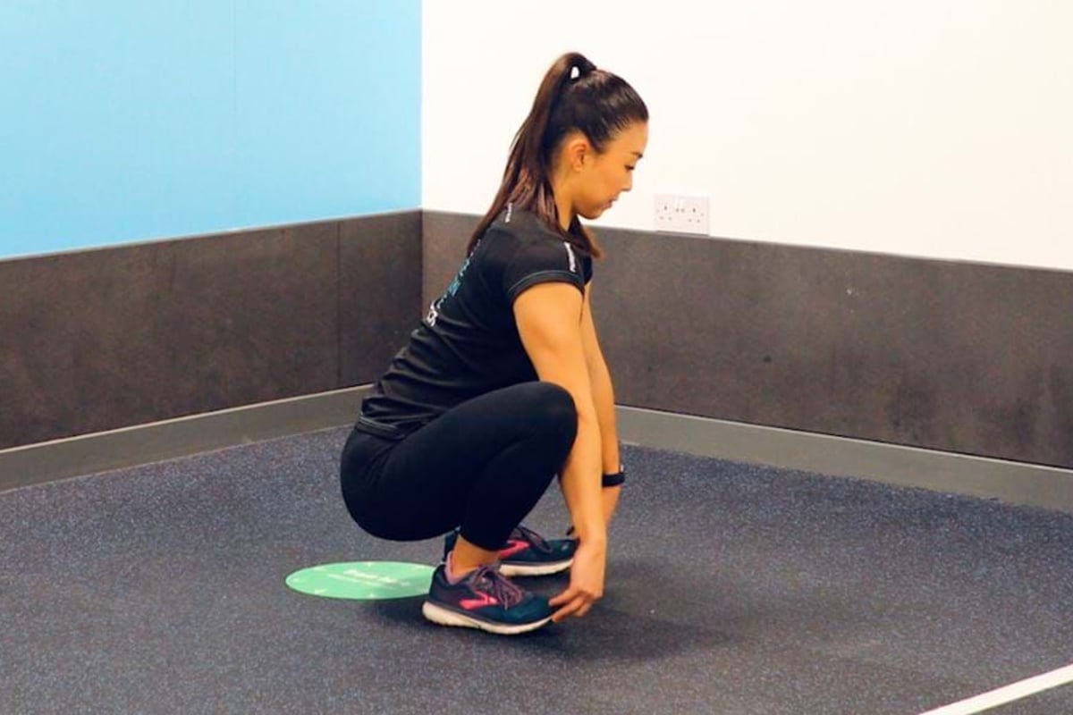 Woman in sportswear squatting and touching her toes in a gym corner