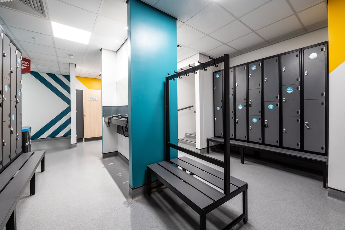 PureGym Peterborough Serpentine Green Shopping Centre: Lockers, benches, and blue partition wall in a gym changing room.