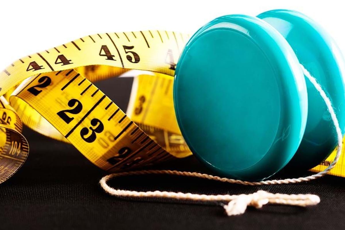 Blue yo-yo with white string next to a yellow measuring tape on black surface